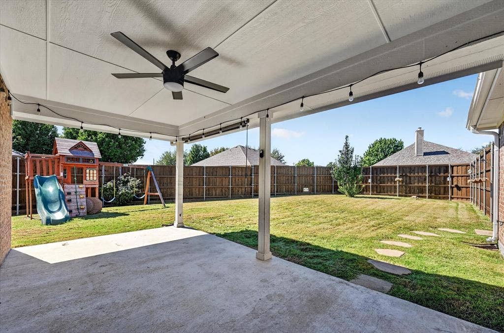 209 Northridge Drive, Wylie, TX 75098 Expansive covered patio with ceiling fan and concrete flooring overlooking a large fenced yard with mature landscaping, wooden play structure, and swing set
