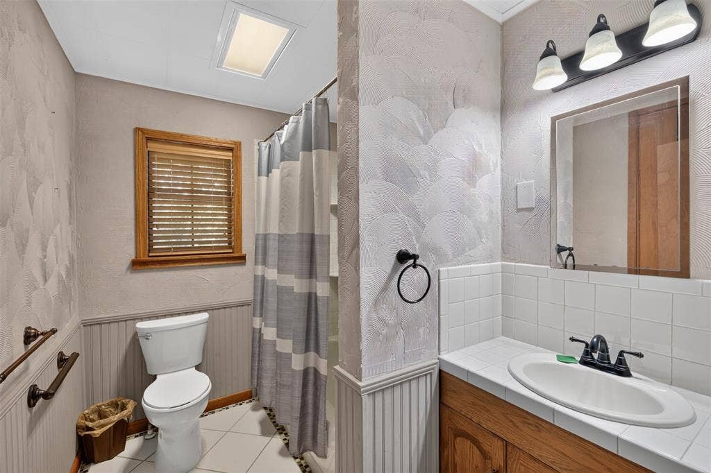 9468 Ranch Lane, Shreveport, LA 71106 Bathroom featuring a vanity with an integrated sink, wood-finish cabinetry, white tile countertop, and a window with wood trim