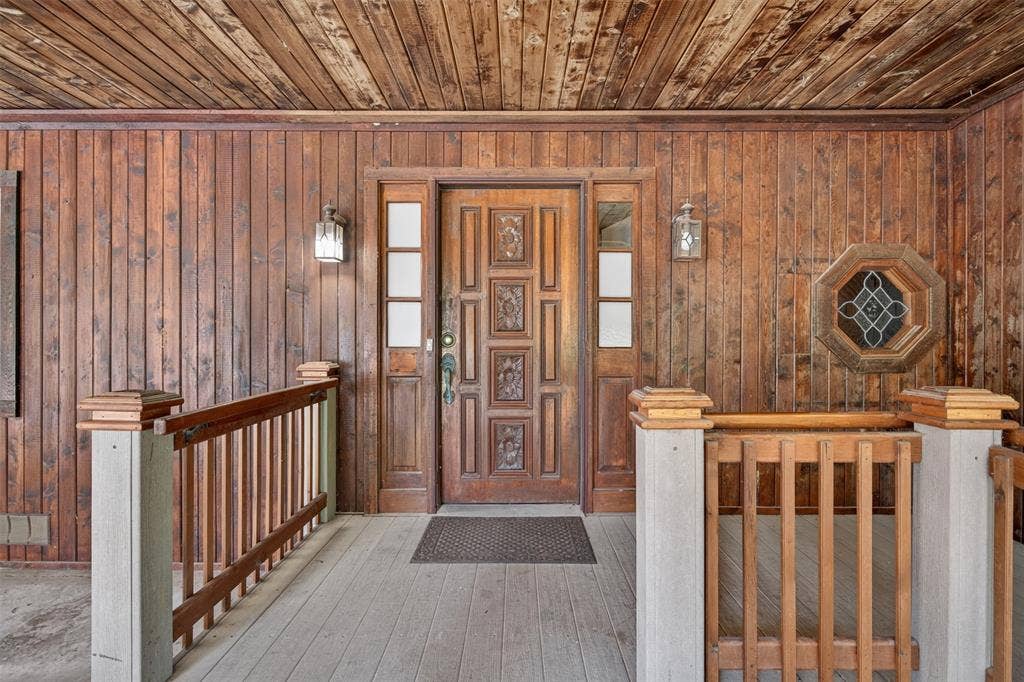 9468 Ranch Lane, Shreveport, LA 71106 Carved wood entry door, wood-paneled walls, wood plank flooring, decorative octagon-shaped window, and wall-mounted exterior light fixtures