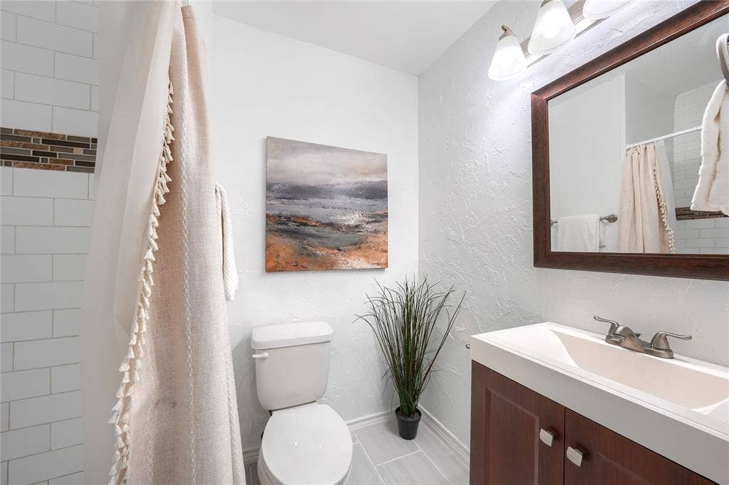1600 Brentwood Drive, Irving, TX 75061 White subway tile shower with decorative accent, wood-finish vanity, integrated white sink, and framed mirror