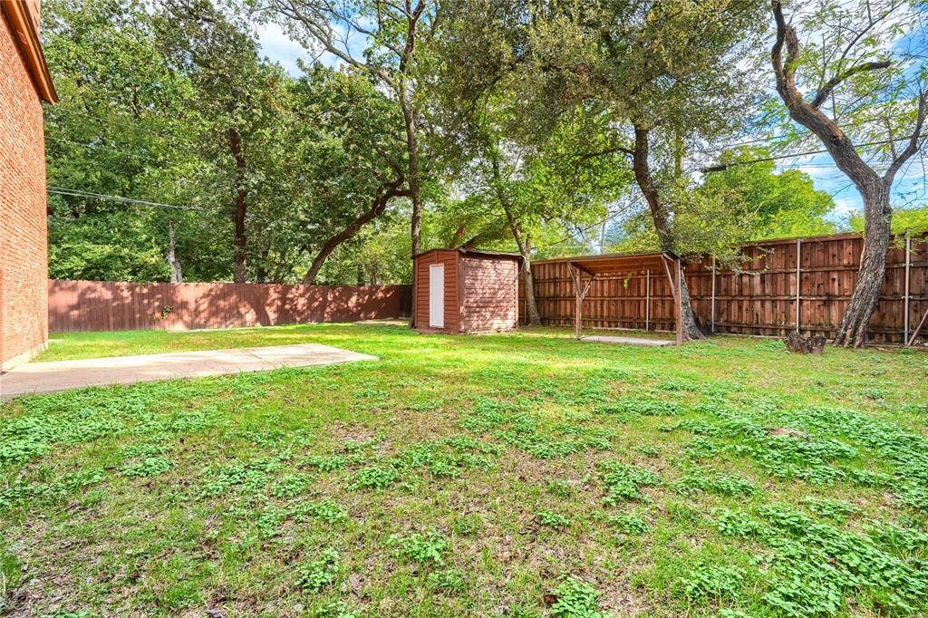 1600 Brentwood Drive, Irving, TX 75061 Expansive yard featuring mature trees, a privacy fence, a storage shed, and a covered patio area