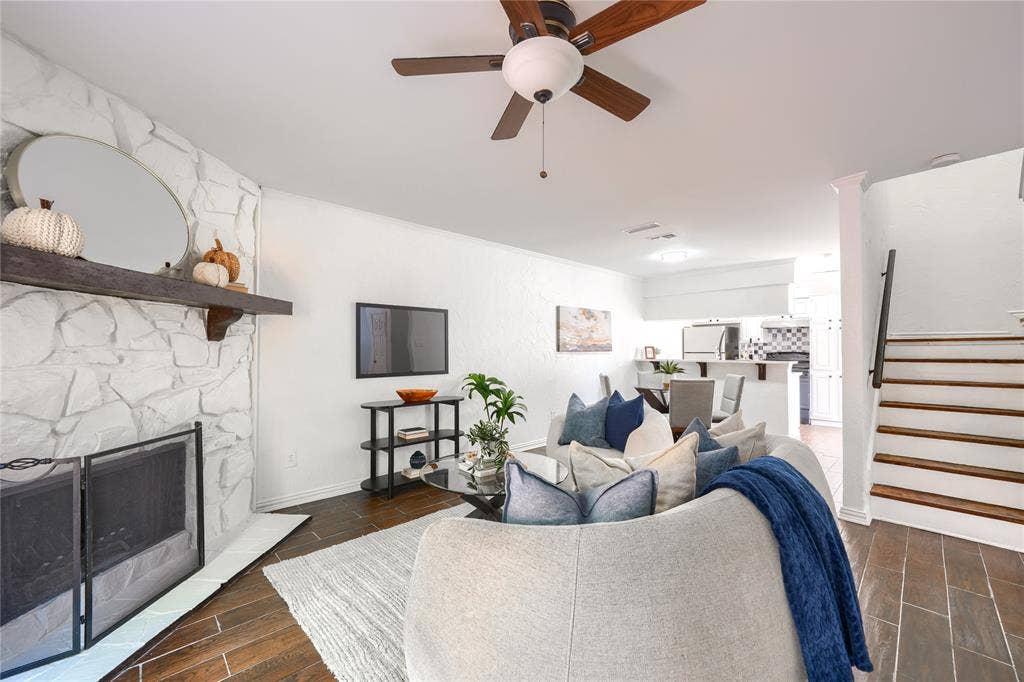 1600 Brentwood Drive, Irving, TX 75061 White stone fireplace with a wood mantel, wood-finish flooring, ceiling fan, and staircase with a dark handrail