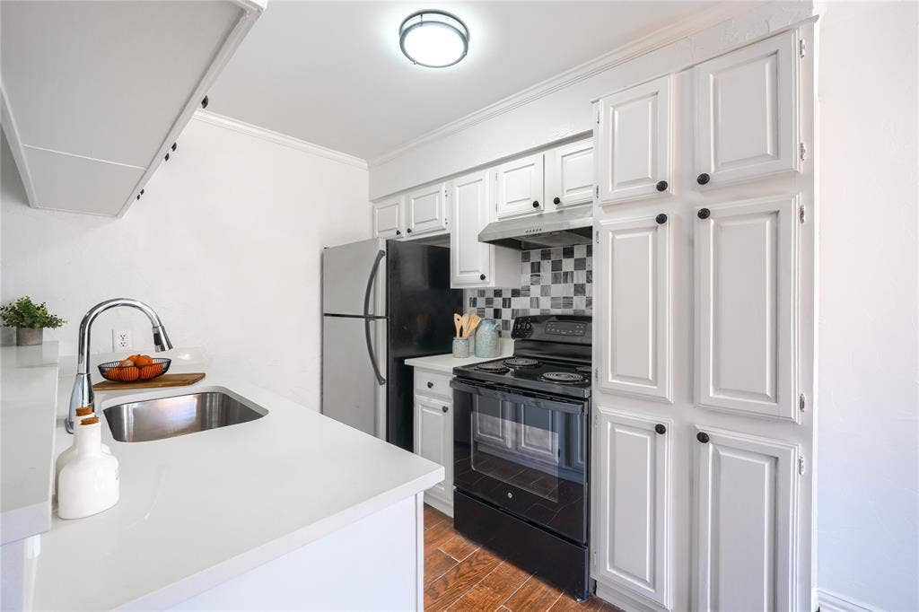 1600 Brentwood Drive, Irving, TX 75061 White cabinetry with black hardware, stainless steel sink, black range with range hood, stainless steel refrigerator, and wood-finish flooring