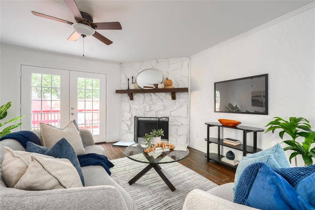 1600 Brentwood Drive, Irving, TX 75061 Wood-finish flooring, white stone-clad fireplace with mantel, white French doors, and ceiling fan with integrated lighting