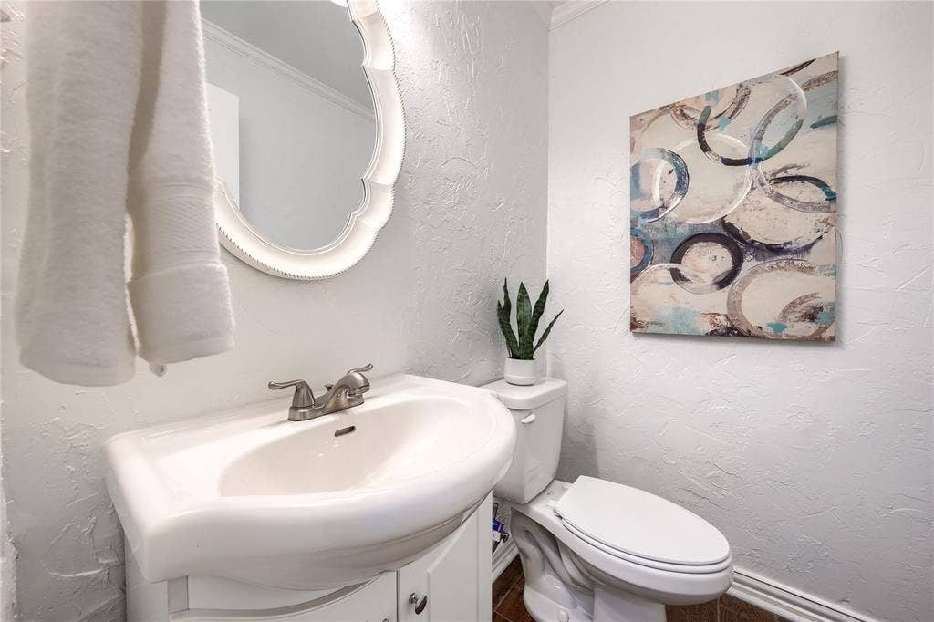 1600 Brentwood Drive, Irving, TX 75061 White pedestal sink with a dual-handle faucet, white toilet, and white framed mirror