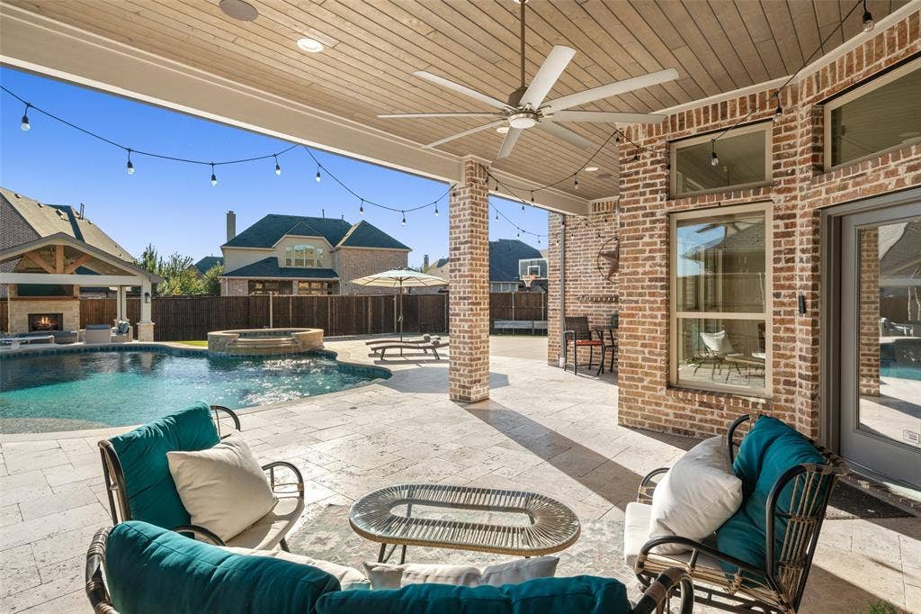 Expansive outdoor living area featuring a covered patio, brick columns, a built-in outdoor kitchen, an inground pool with an integrated spa, and an outdoor fireplace