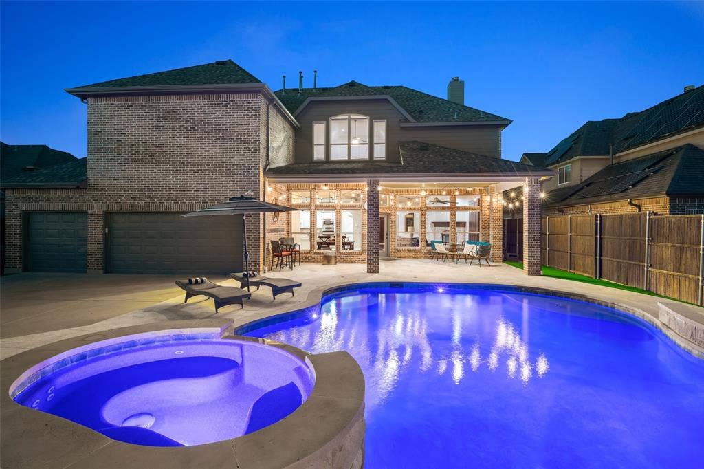Stunning brick Colonial with illuminated resort-style backyard featuring a lagoon-shaped saltwater pool with integrated spa, travertine decking, and mature landscaping