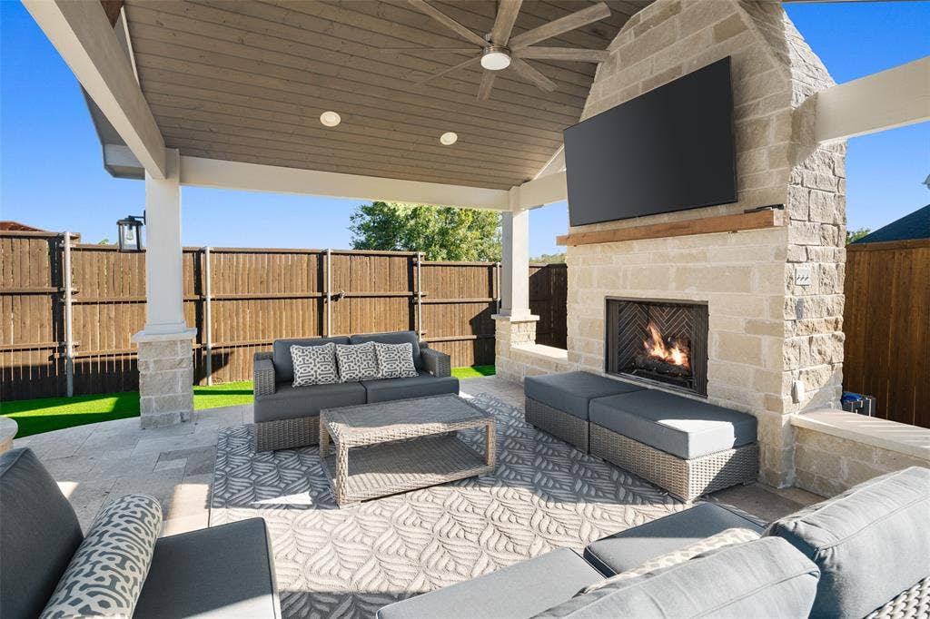 Covered outdoor patio featuring a stone fireplace with wood mantel, a ceiling fan, and recessed lighting