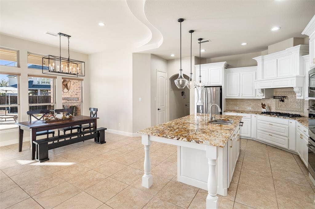 Gourmet kitchen featuring white cabinetry, stainless steel appliances, a large island with a composite countertop, and pendant lighting