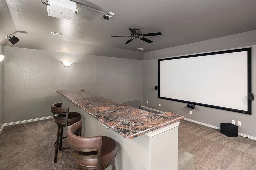 Integrated projection screen, ceiling-mounted projector, built-in bar with stone countertop, ceiling fan, and recessed lighting