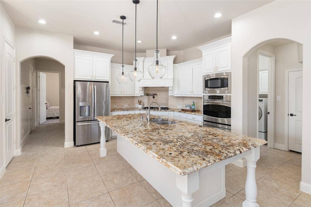 Kitchen featuring a large island with a stone countertop, white cabinetry, stainless steel appliances, and pendant lighting