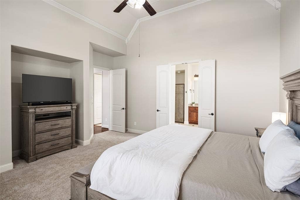 Vaulted ceilings with crown molding, ceiling fan, carpet flooring, built-in media niche, and double doors