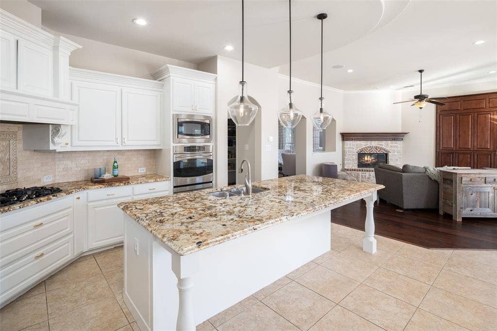 Kitchen with granite countertops, stainless steel built-in appliances, a gas cooktop, white cabinetry, and a large central island with pendant lighting