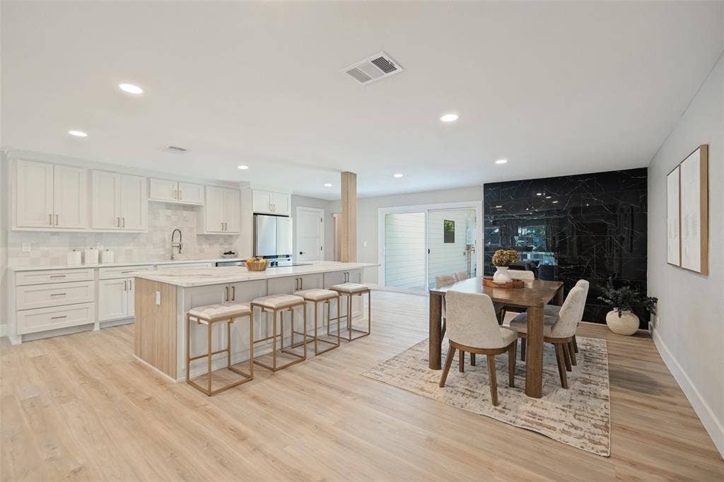 3129 Flowerdale Lane, Dallas, TX 75229 Open-concept living space featuring a kitchen with white cabinetry, a large island with seating, a patterned tile backsplash, and wood-finish flooring