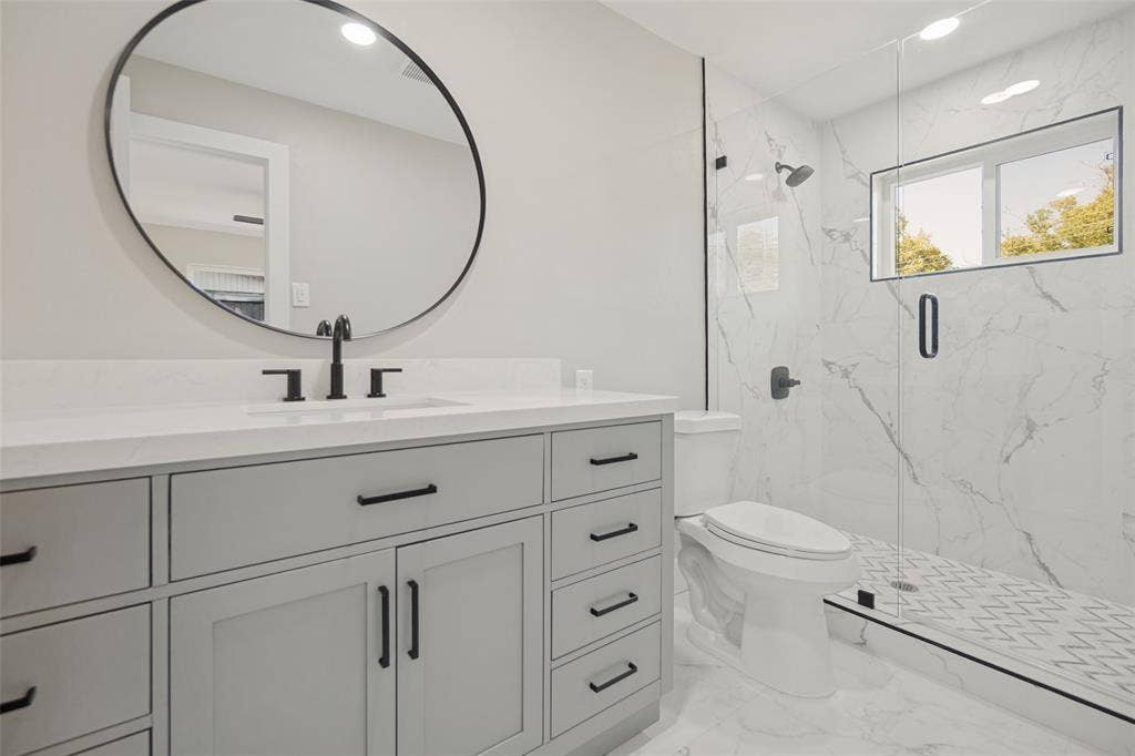 3129 Flowerdale Lane, Dallas, TX 75229 Floating vanity with a quartz countertop, circular mirror, and matte black fixtures