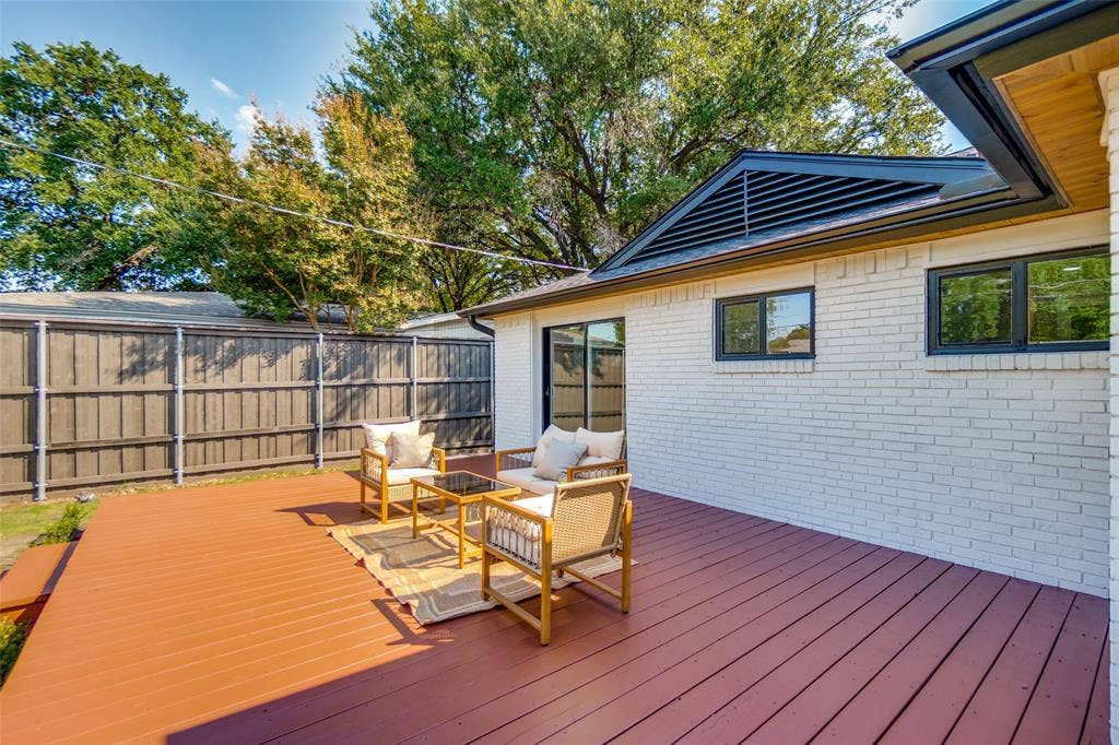 3129 Flowerdale Lane, Dallas, TX 75229 Expansive rear deck, white brick exterior, black frame windows, and dark louvered gable vent