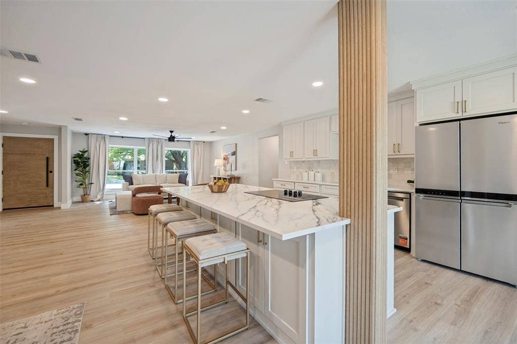 3129 Flowerdale Lane, Dallas, TX 75229 Open-concept living space featuring wood-finish flooring, a kitchen island with stone countertop, built-in cooktop, and a stainless steel refrigerator