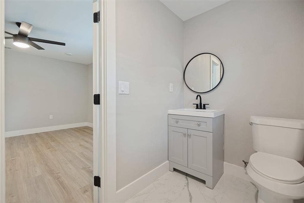 3129 Flowerdale Lane, Dallas, TX 75229 Light gray vanity with an integrated sink, matte black faucet, and a round black-framed mirror