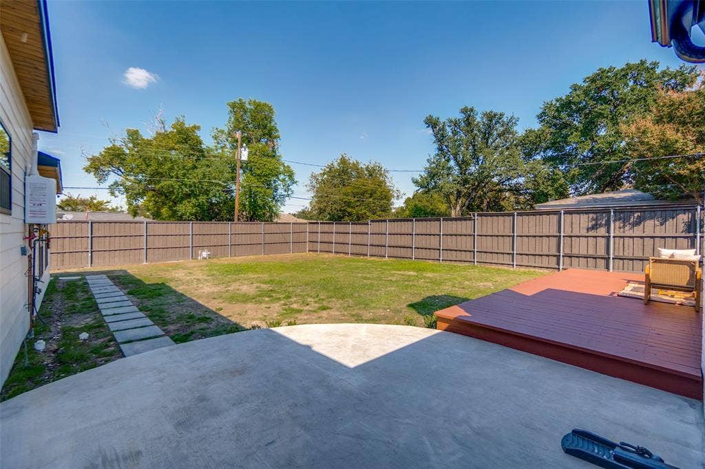 3129 Flowerdale Lane, Dallas, TX 75229 Expansive backyard featuring a concrete patio, a raised wood deck, a full privacy fence, a manicured lawn, and mature trees