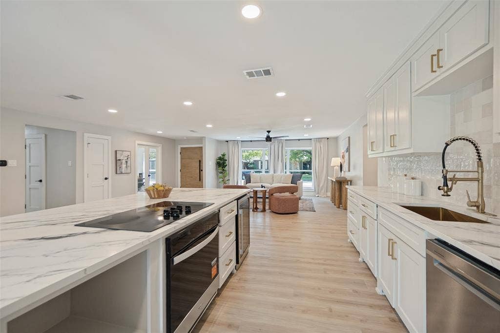 3129 Flowerdale Lane, Dallas, TX 75229 Kitchen featuring an expansive island with cooktop, white cabinetry with gold-tone hardware, stainless steel appliances, and wood-finish flooring