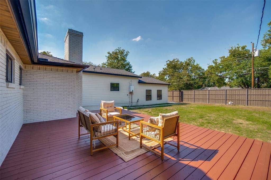 3129 Flowerdale Lane, Dallas, TX 75229 Expansive wood deck with a red-brown finish, white brick exterior, black gutters, and a gray stone chimney
