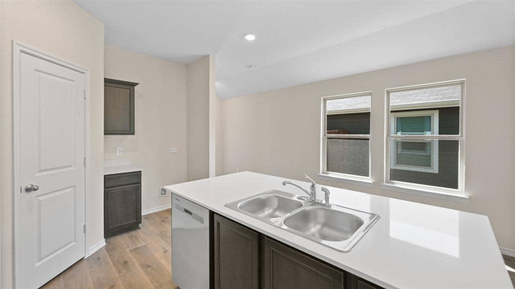 5431 Cormorant Grove, Crandall, TX 75114 Kitchen island featuring a dual-basin stainless steel sink with a chrome faucet, white countertop, and integrated dishwasher