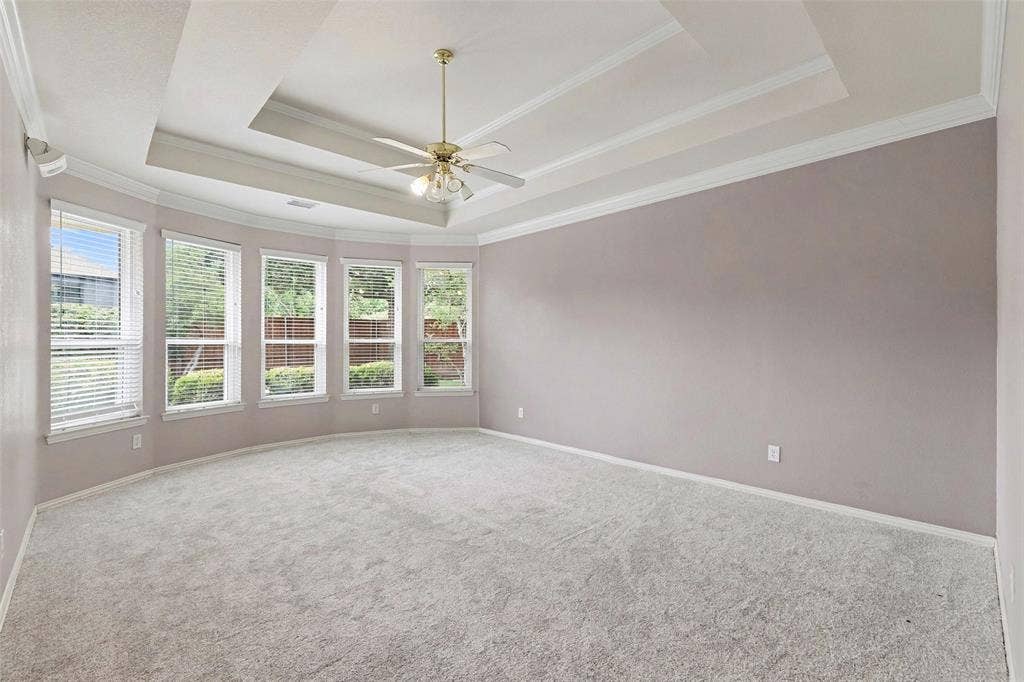 7813 San Isabel Drive, Plano, TX 75025 Recessed tray ceiling with crown molding, ceiling fan with integrated lighting, multiple windows with blinds, and light-toned carpet flooring