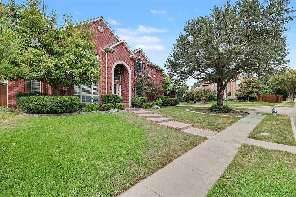 7813 San Isabel Drive, Plano, TX 75025 Red brick exterior with an arched entry, mature trees, landscaped shrubbery, and a concrete sidewalk