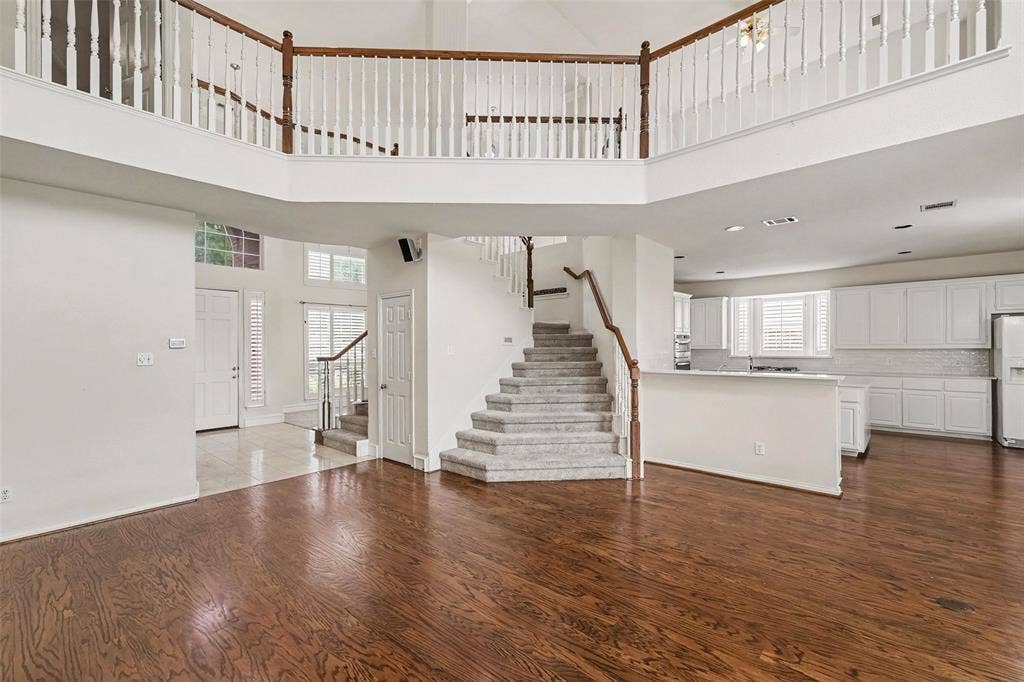 7813 San Isabel Drive, Plano, TX 75025 Hardwood flooring, two-story entryway, grand staircase with wood railing, white kitchen cabinetry, and a second-story interior balcony