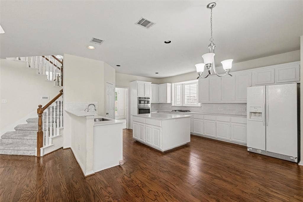 7813 San Isabel Drive, Plano, TX 75025 Hardwood flooring, white cabinetry, kitchen island, built-in appliances, and staircase with wood handrail