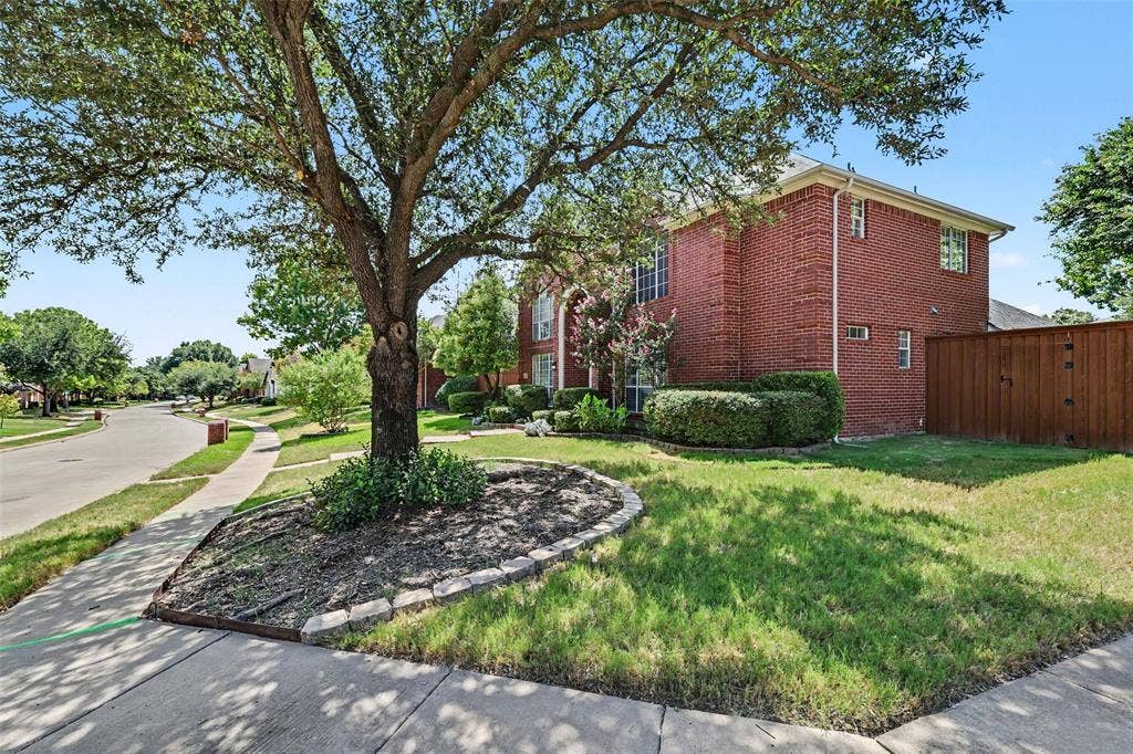 7813 San Isabel Drive, Plano, TX 75025 Red brick facade, mature tree with stone-edged planting bed, manicured shrubbery, wood fence, and sidewalk access