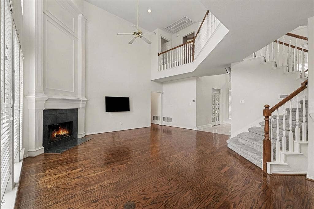 7813 San Isabel Drive, Plano, TX 75025 Hardwood flooring throughout, a soaring two-story ceiling, a fireplace with a stone surround, and an open staircase with a carpeted runner