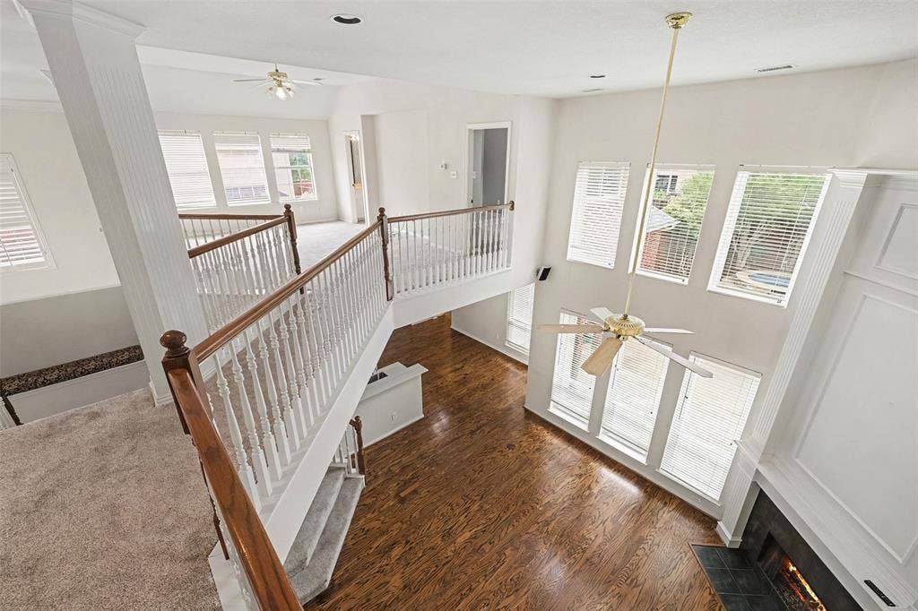 7813 San Isabel Drive, Plano, TX 75025 Two-story living area with wood-finish flooring, a fireplace with a dark stone hearth, and multiple windows
