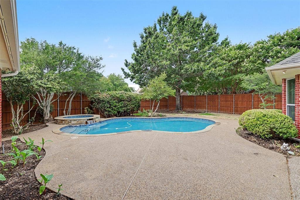 7813 San Isabel Drive, Plano, TX 75025 Backyard featuring a free-form swimming pool with integrated spa, concrete decking, wood fencing, and mature landscaping
