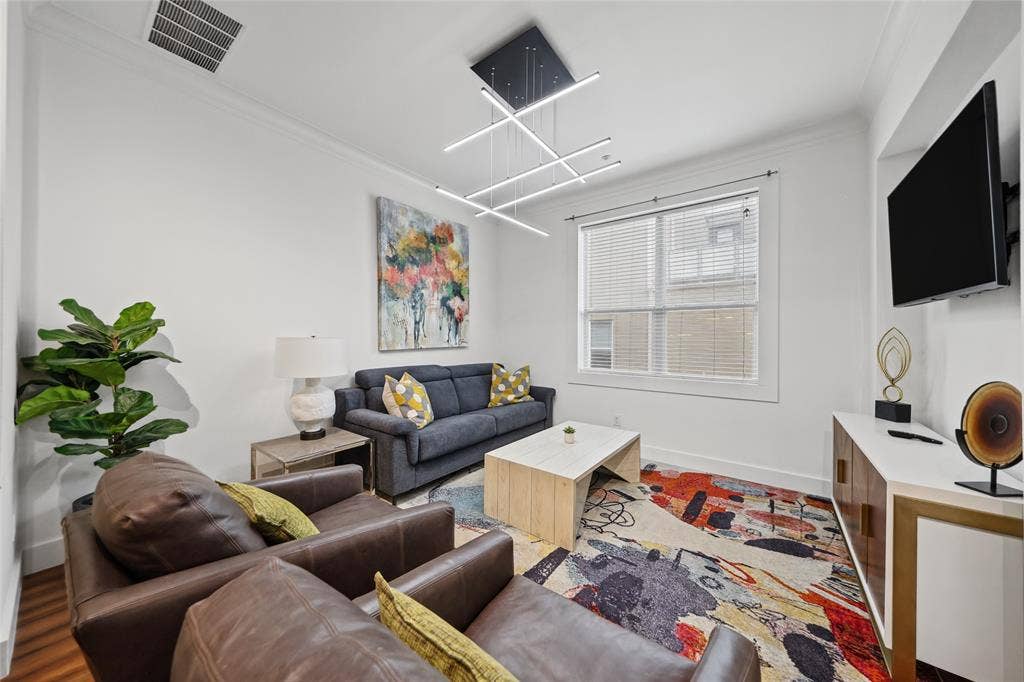 4312 Mckinney Avenue, #4, Dallas, TX 75205 White walls complemented by crown molding, wood-finish flooring, modern linear pendant lighting, and a built-in media console with gold accents