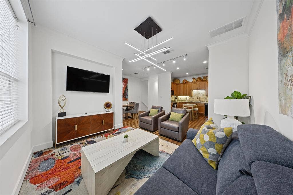 4312 Mckinney Avenue, #4, Dallas, TX 75205 Open-concept living space featuring a wall-mounted flat-screen television, wood-finish cabinetry with storage, modern linear ceiling fixture, recessed lighting, and a wood-finish kitchen with integrated appliances visible in the background