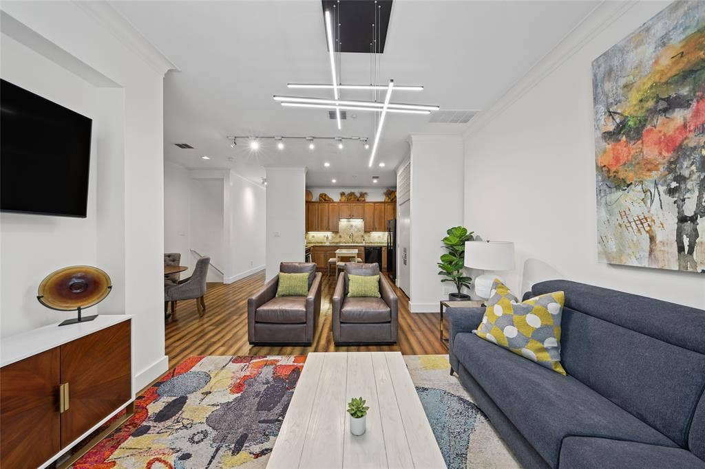4312 Mckinney Avenue, #4, Dallas, TX 75205 Modern open-concept living space featuring hardwood flooring, recessed and linear ceiling lighting, a gray upholstered sofa with accent pillows, a wood-finish media console with mounted flat-screen television, and a colorful area rug anchoring the seating arrangement