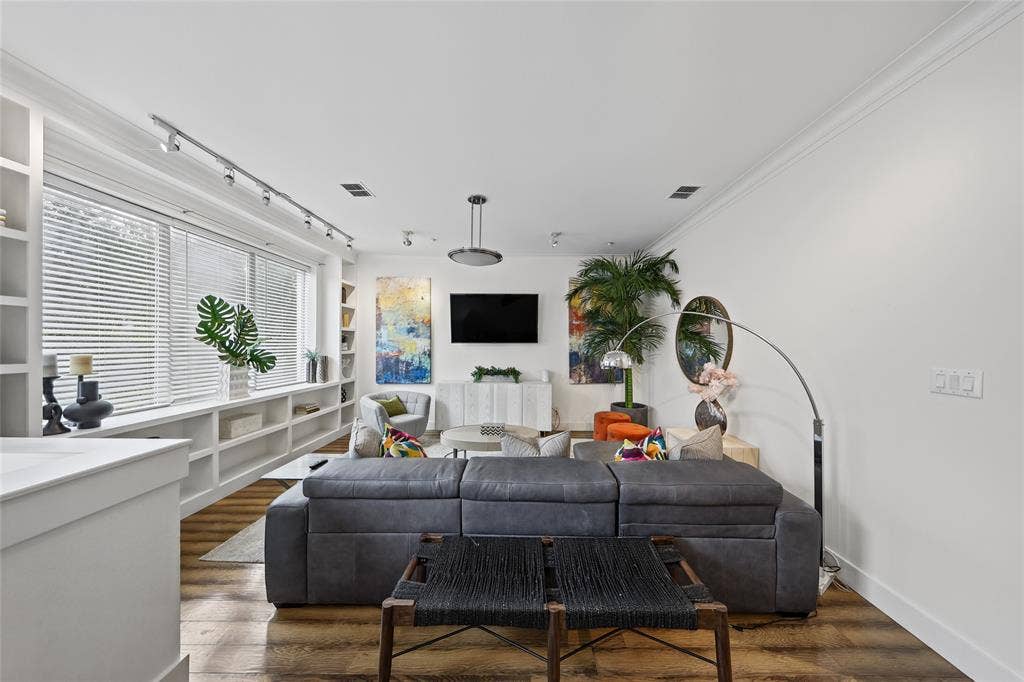 4312 Mckinney Avenue, #4, Dallas, TX 75205 Bright, open living room showcasing hardwood flooring, a gray upholstered sectional sofa, and a wall-mounted flat-screen television above a white built-in fireplace surround