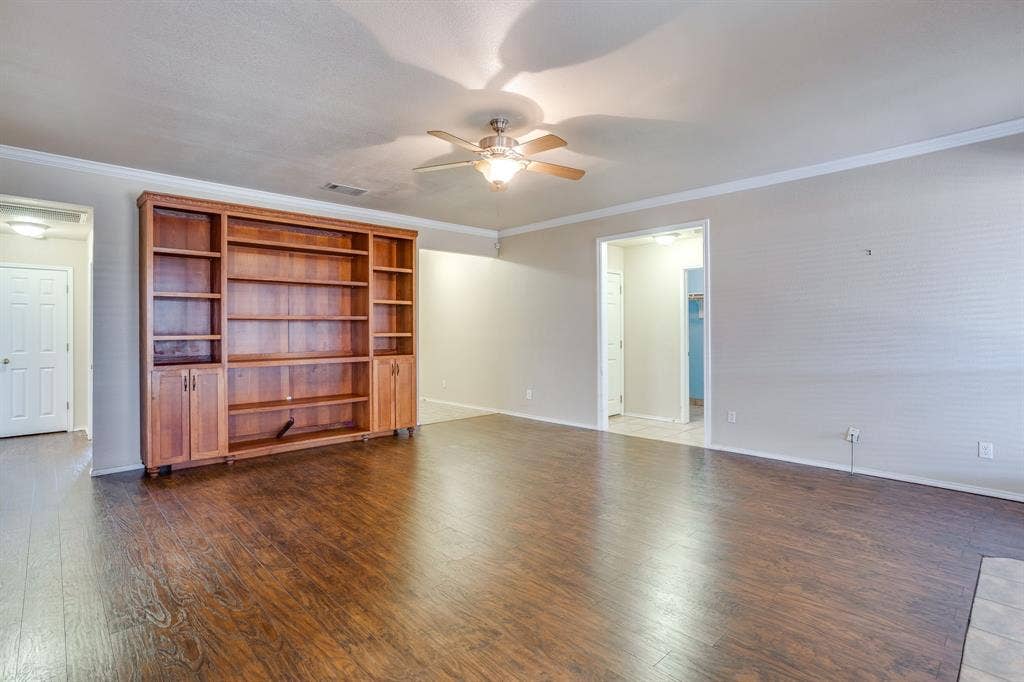 Wood-finish flooring, built-in shelving with cabinetry, crown molding, and ceiling fan with lighting