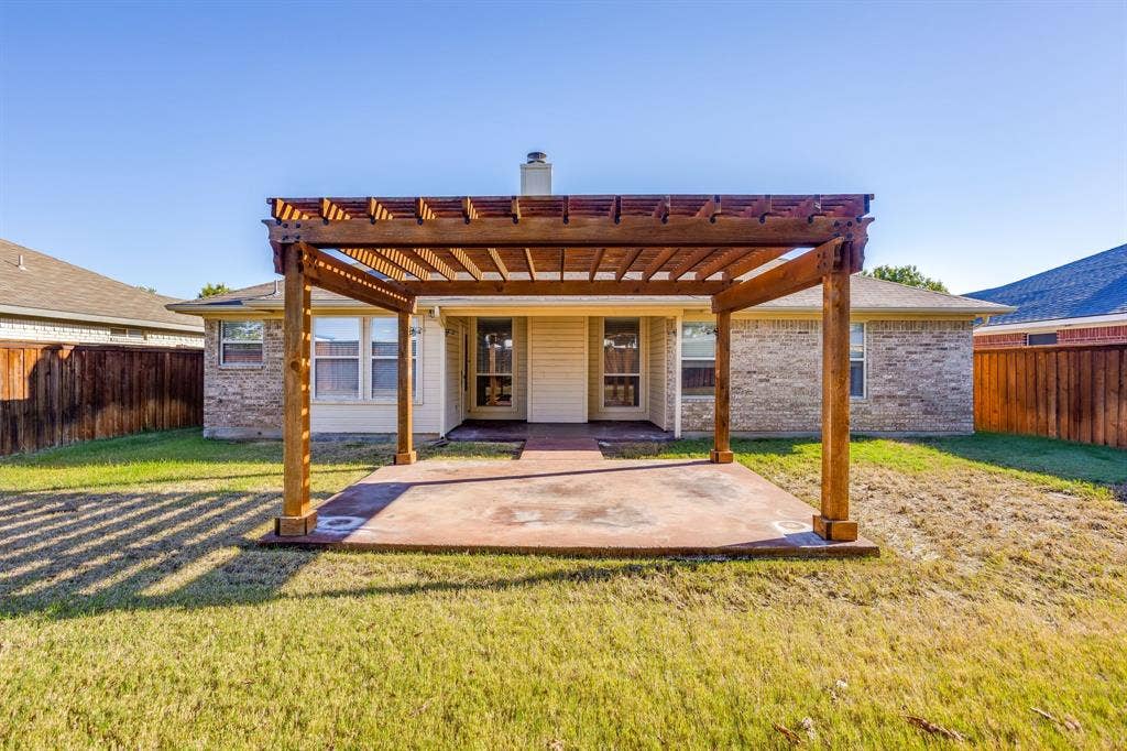 Expansive backyard featuring a stained concrete patio, wooden pergola, and a privacy fence
