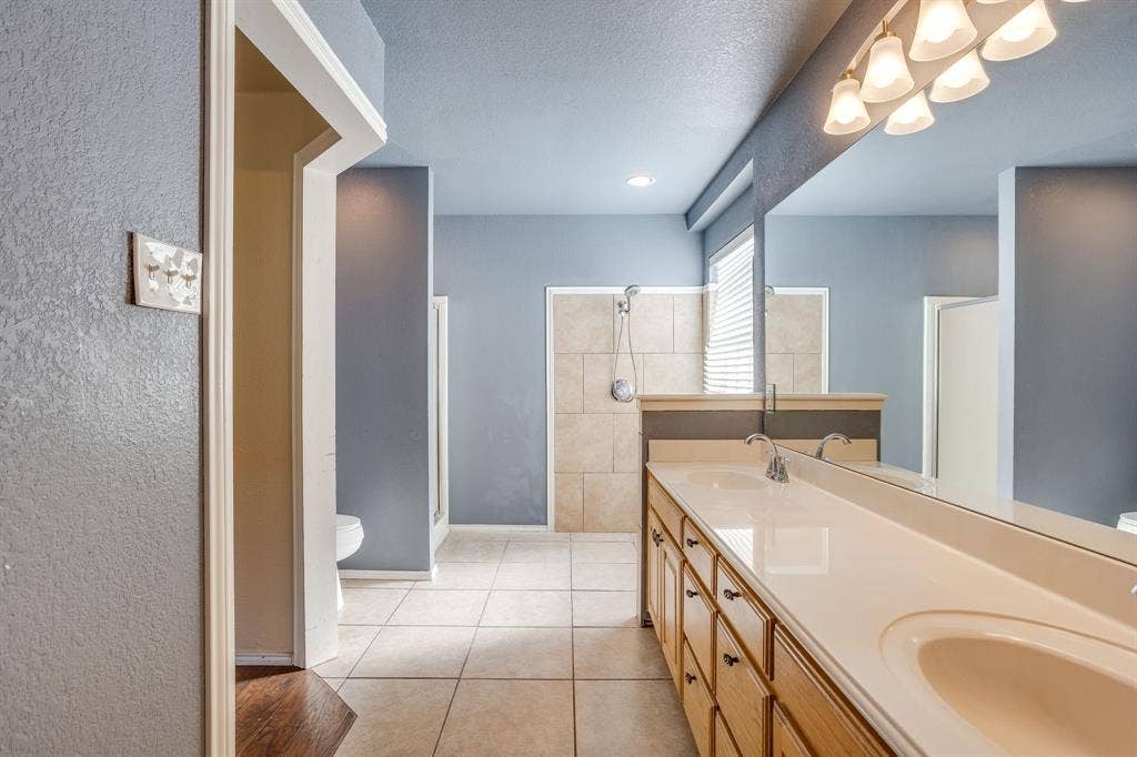 Dual vanity with integrated sinks, full-width mirror, tile flooring, and a tiled shower enclosure