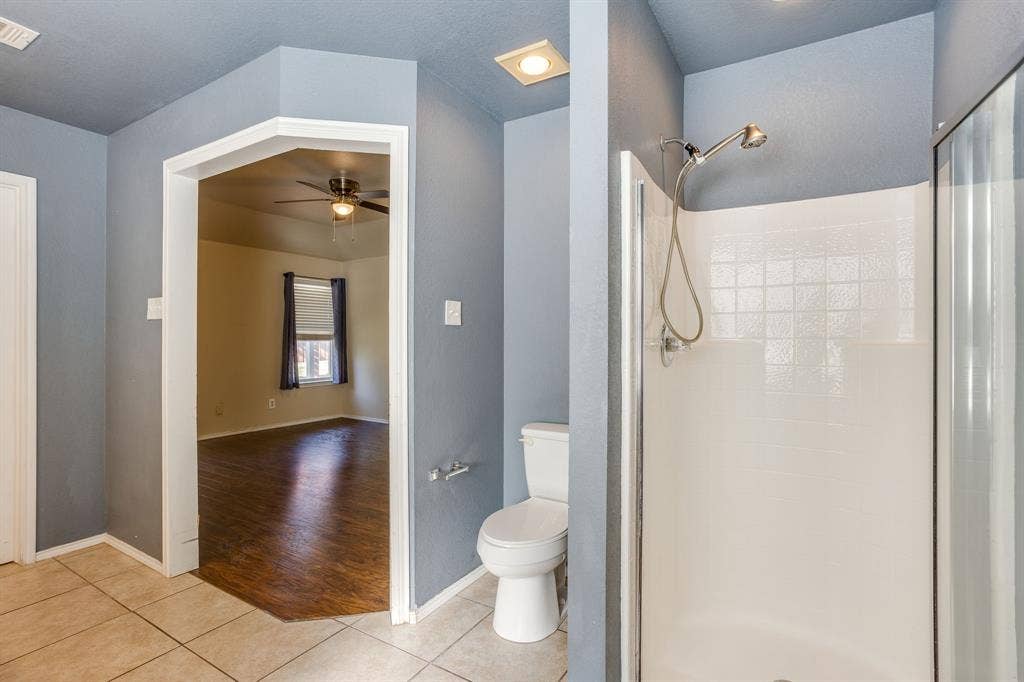 Shower enclosure with white tile surround, ceramic toilet, and tiled flooring