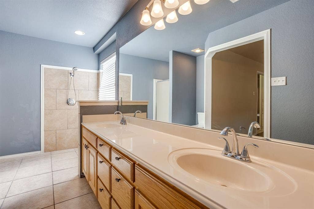 Dual vanity with integrated sinks and chrome fixtures, ample storage cabinetry, and a spacious mirror