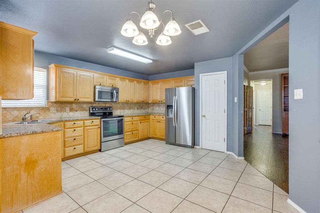 Kitchen featuring wood cabinetry, stainless steel appliances, tile flooring, and a decorative chandelier