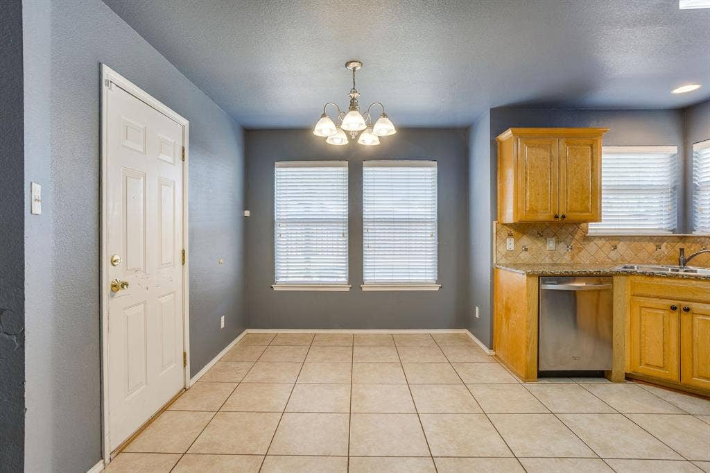 Tiled flooring, warm wood cabinetry, stainless steel dishwasher, decorative tile backsplash, and a ceiling-mounted lighting fixture