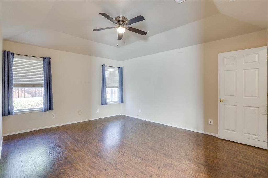 Tray ceiling with ceiling fan, wood-finish flooring, and two windows