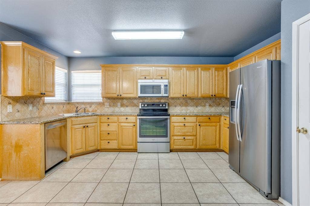 Kitchen featuring wood cabinetry, stainless steel appliances, tile flooring, and a tile backsplash