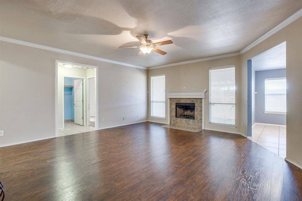 Wood-finish flooring, ceiling fan, fireplace with tile surround, and multiple windows with blinds