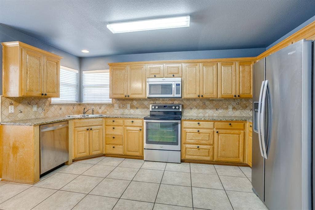 Kitchen featuring wood cabinetry, stainless steel appliances, granite countertops, and tiled flooring