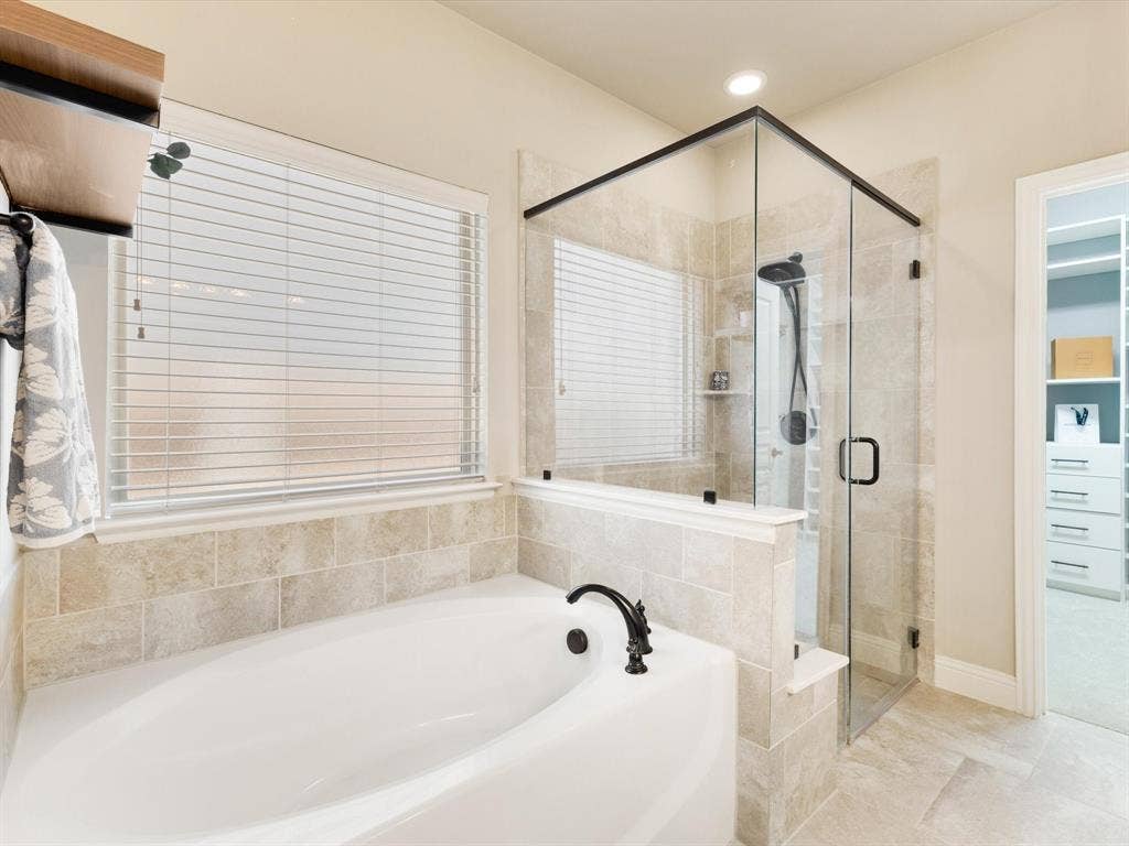1020 Fallon Drive, McKinney, TX 75071 Built-in soaking tub with a black arch faucet, glass-enclosed shower with black hardware, and tiled walls and flooring
